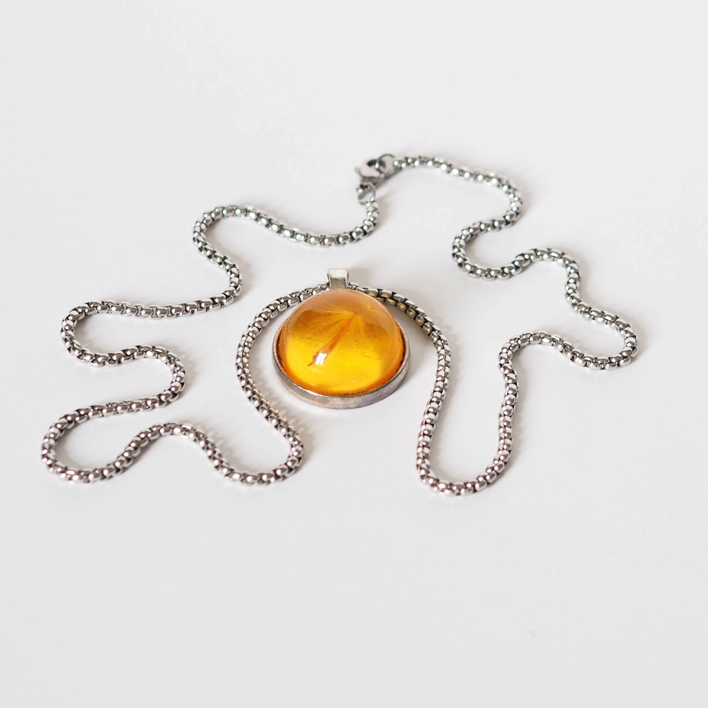 PENDANT WITH A FLYING SEED INSIDE AMBER RESIN.
