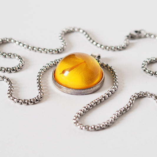 PENDANT WITH A FLYING SEED INSIDE AMBER RESIN.